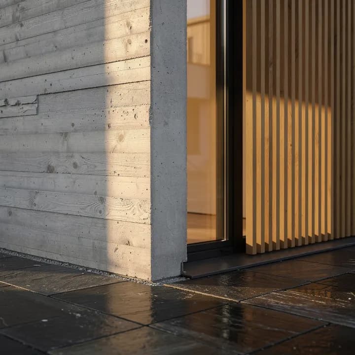 FLUX.2 Pro: board-formed concrete corner with oak slats, a lit window and wet stone paving
