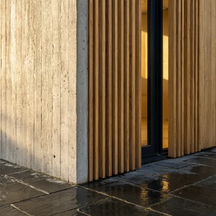 Qwen Image 3: board-formed concrete corner with oak slats, a lit window and wet stone paving